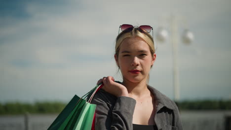 white woman in grey shirt and sunglasses carries shopping bags over her shoulder, facing slightly backward with a focused expression, the background is blurred, featuring an electric pole