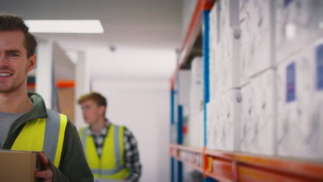 portrait of smiling male worker wearing high vis safety vest holding box inside warehouse