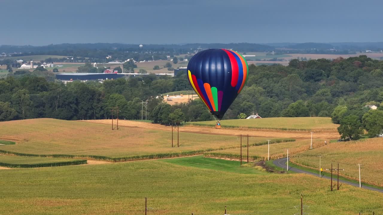 Mongolfiera colorata che vola lentamente sopra la periferia della città americana nei campi verdi con il cielo sullo sfondo, ripresa aerea con drone