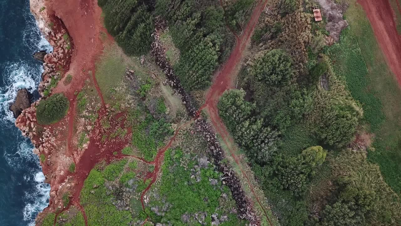 Drone flying up above old rock wall, dirt road, and ocean cliffs in Kauai, Hawaii