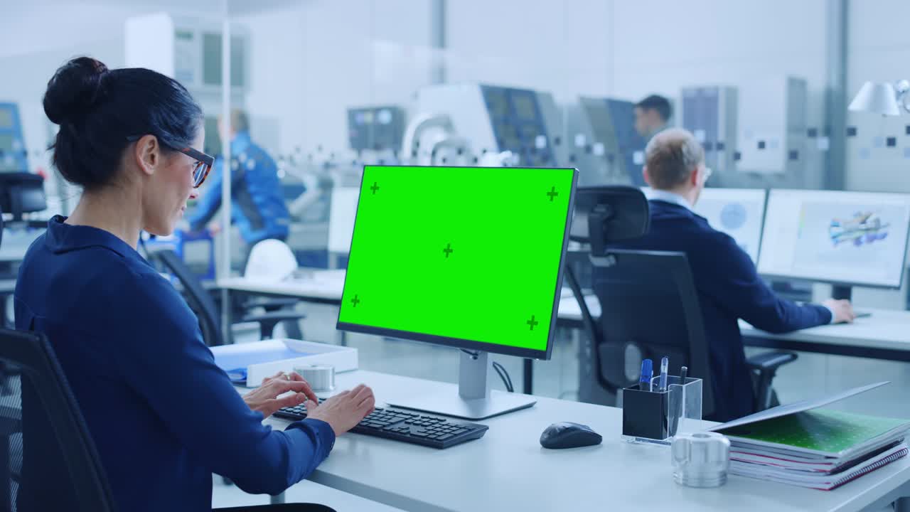 어깨 위: 개인 컴퓨터에서 일하는 여성 수석 엔지니어, 디스플레이는 녹색 모형 화면 또는 크로마 키입니다. 첨단 기술 기계와 전문 노동자를 가진 산업 공장