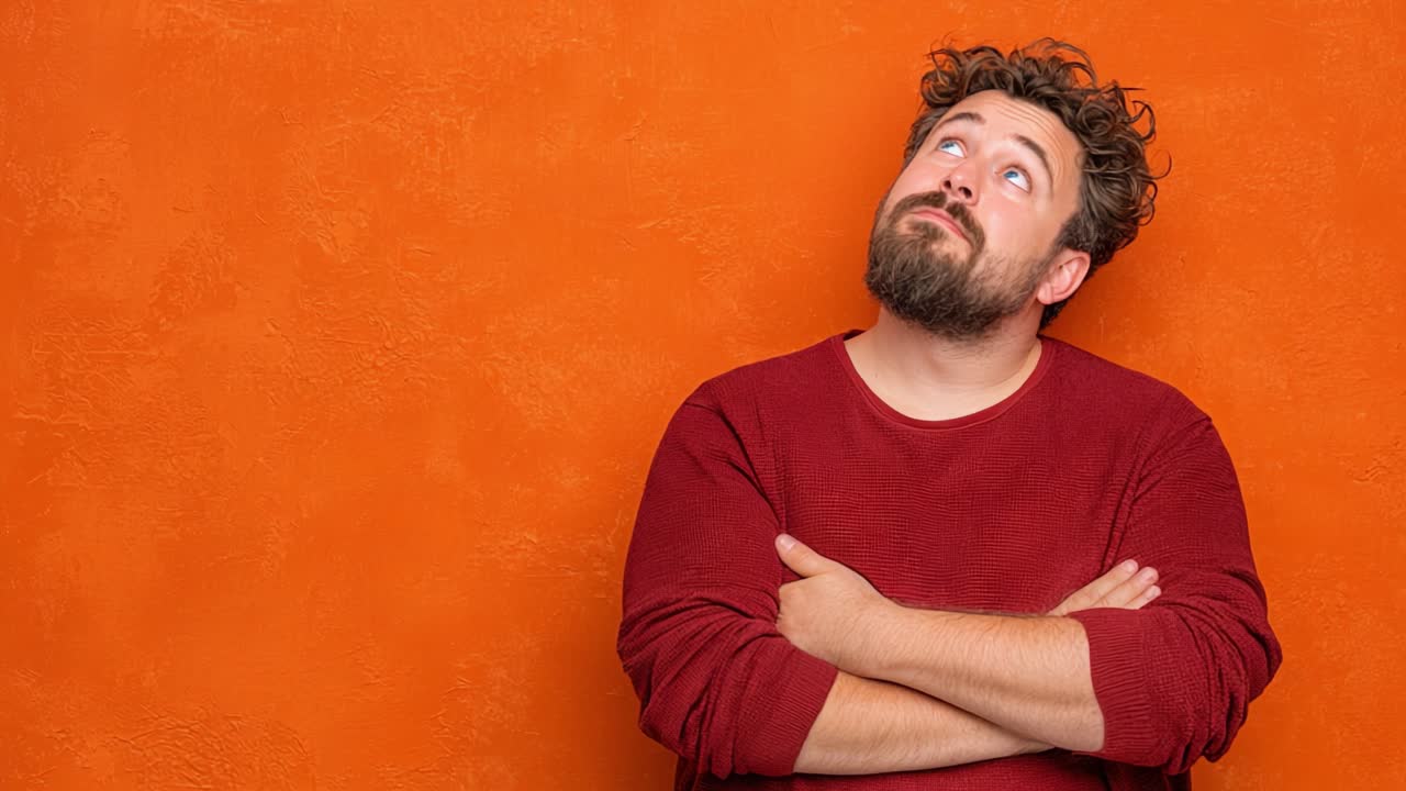 Un Uomo Pensieroso con un Maglione Accogliente Guarda Verso l'Alto Contro una Vivace Parete Arancione, Catturando un Momento di Contemplazione e Curiosità in un Contesto Giocoso