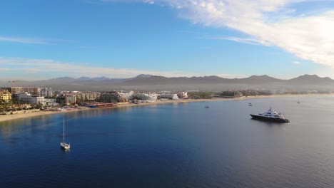 Zoom-in-over-the-bahia-of-Cabo-San-Lucas-Mexico-at-the-sunrise,-Luxury-Yatch-and-Sailboats-at-the-coast