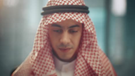 portrait of young successful arab businessman in traditional outfit gently smiling, wearing white kandura and black agal keeping a ghutra in place. saudi, emirati, arab businessman concept.