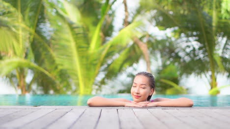 Mujer-Asiática-Disfruta-De-Un-Día-Soleado-Dentro-Del-Agua-De-La-Piscina-Del-Paraíso-Tropical-Con-Palmeras-En-El-Fondo