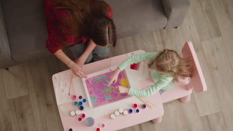 woman and girl add bright colors to pattern on oily water