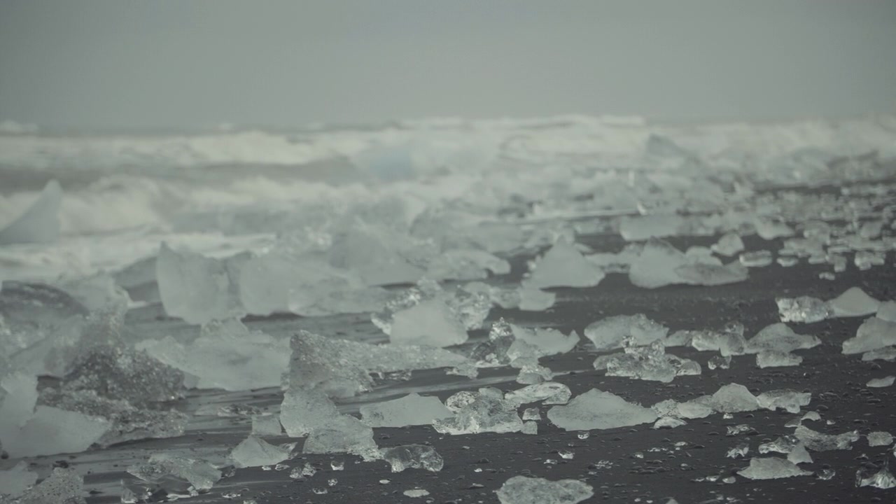 Trozos de hielo en una playa de arena negra con olas del océano