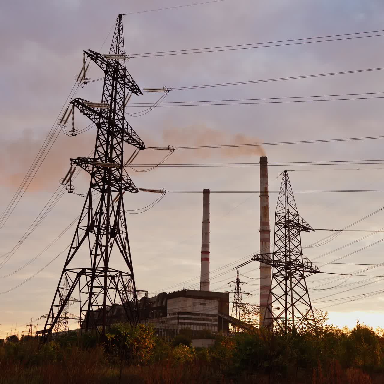 Electricity pylons bearing the power supply across a rural landscape during sunset. Selective focus