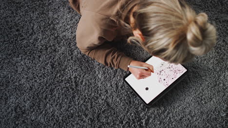 overhead shot of woman drawing on digital tablet using stylus pen at home