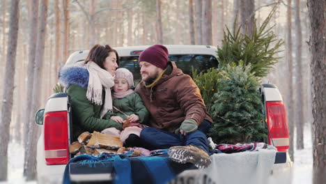 una joven familia feliz preparándose para la mañana de navidad sentada en la parte trasera del auto después de un