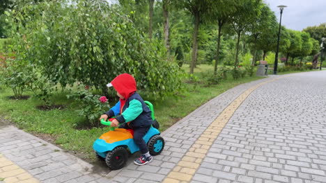adorable little boy wearing a jacket with hood riding toy car. caucasian toddler having active time in the park.