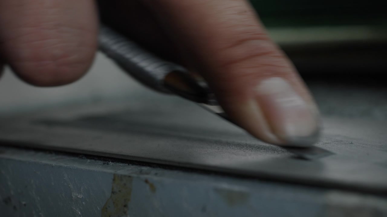 Primer plano de mano cortando material con cuchilla en banco de trabajo en proceso de producción de calzado