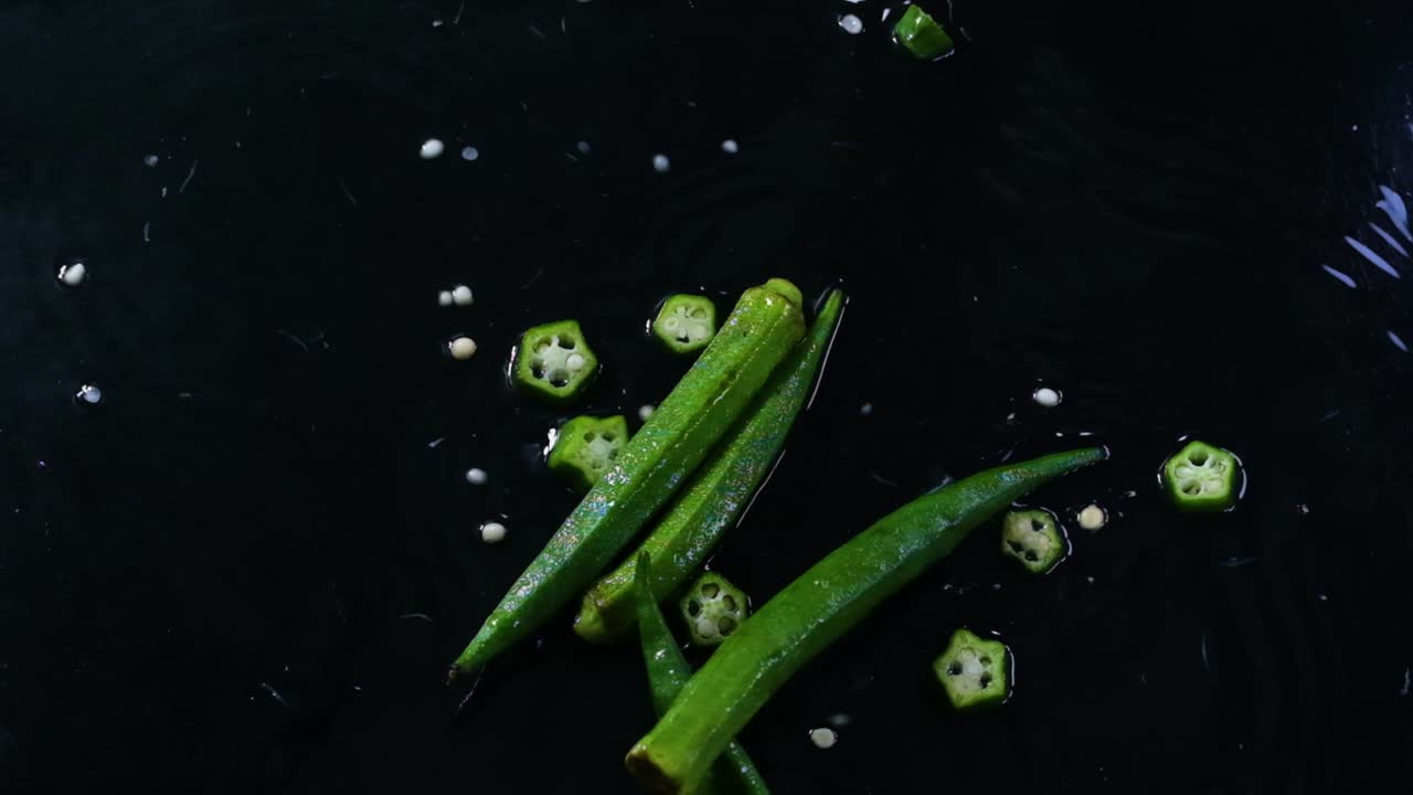 Whole and sliced okra, or lady's fingers, fall on a wet surface