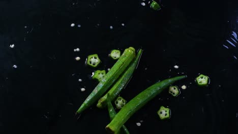 la okra entera y cortada, o los dedos de la dama, caen sobre una superficie húmeda