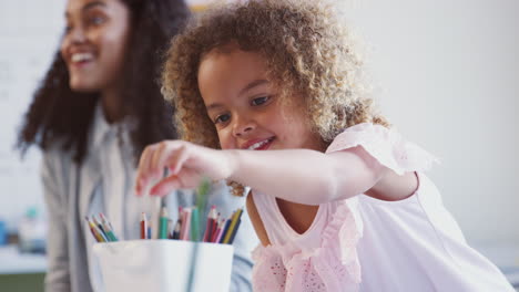 Una-Colegiala-De-Raza-Mixta-Dibujando-En-Un-Aula-De-Escuela-Infantil-Eligiendo-Un-Lápiz,-Enfoque-Selectivo