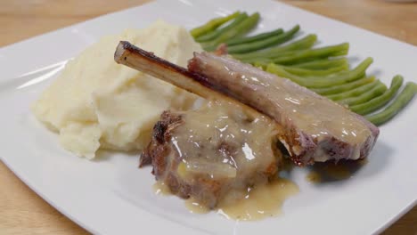 tiro deslizante de chuletas de cordero en un plato blanco con salsa, puré de patata y judías verdes