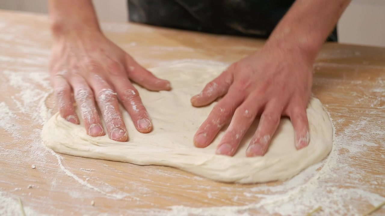 Primo piano di mani che impastano l'impasto della pizza su un tavolo di legno infarinato