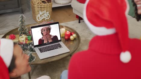 Familia-Diversa-Con-Sombreros-De-Santa-Usando-Una-Computadora-Portátil-Para-Una-Videollamada-Navideña-Con-Una-Mujer-Feliz-En-La-Pantalla