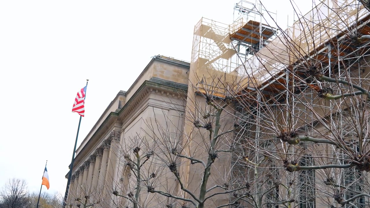 Esterno di un classico edificio in pietra con impalcature da costruzione e bandiere. Facciata di architettura neoclassica in ristrutturazione con impalcature, bandiera americana e alberi spogli a New York City.