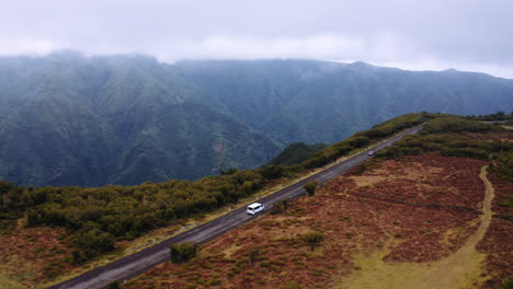 Drohnenfahrt-Eines-Weißen-Lieferwagens,-Der-Auf-Einer-Bergstraße-Mit-Spektakulären-Hügeln-Im-Hintergrund-Fährt