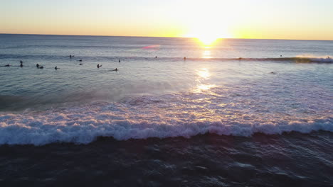 Aerial-view-of-drone-tracking-backwards-following-a-wave-to-shore-as-it-breaks-onto-the-rocks-with-a-beautiful-sunrise-reflecting-at-the-very-popular-Burleigh-Heads-Gold-Coast-QLD-Australia