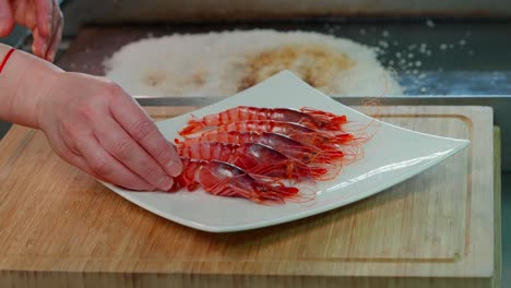 hand-serves-red-shrimp-on-a-plate-on-a-wooden-table