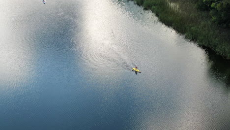 Lonely-person-paddling-yellow-board-in-Aviris-lake-in-Lithuania,-aerial-drone-view