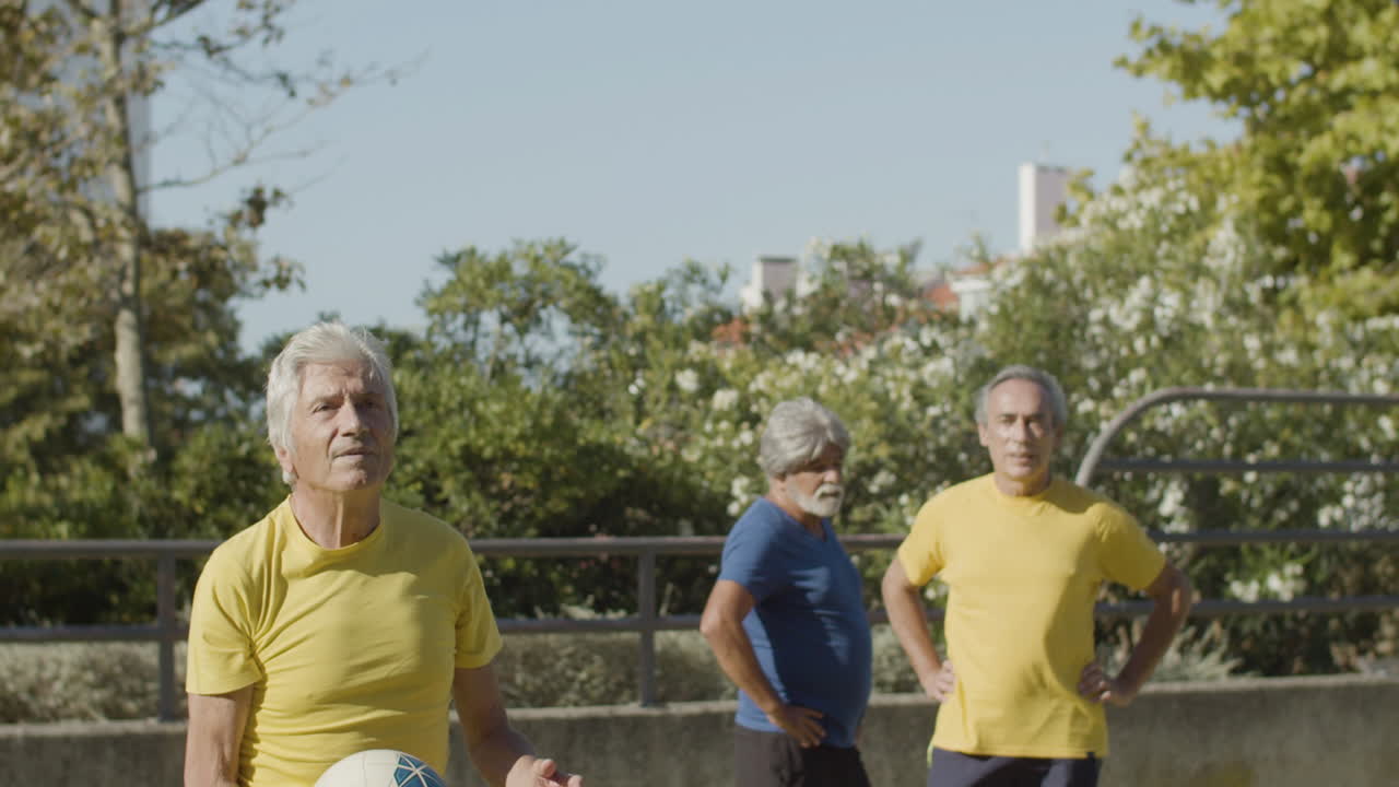 vista frontal de un deportista senior golpeando la pelota con la cabeza mientras entrena con amigos en el estadio