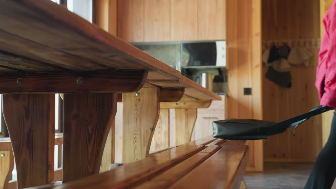 Close up of women retrieving bags from wooden bench in rustic cabin kitchen, showing casual outfits and warm wooden textures with soft daylight