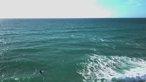 surfers bobbing on top of breaking clear waves