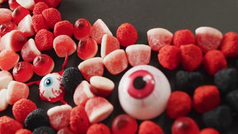 close up of scary eyes toy and halloween candies against grey background