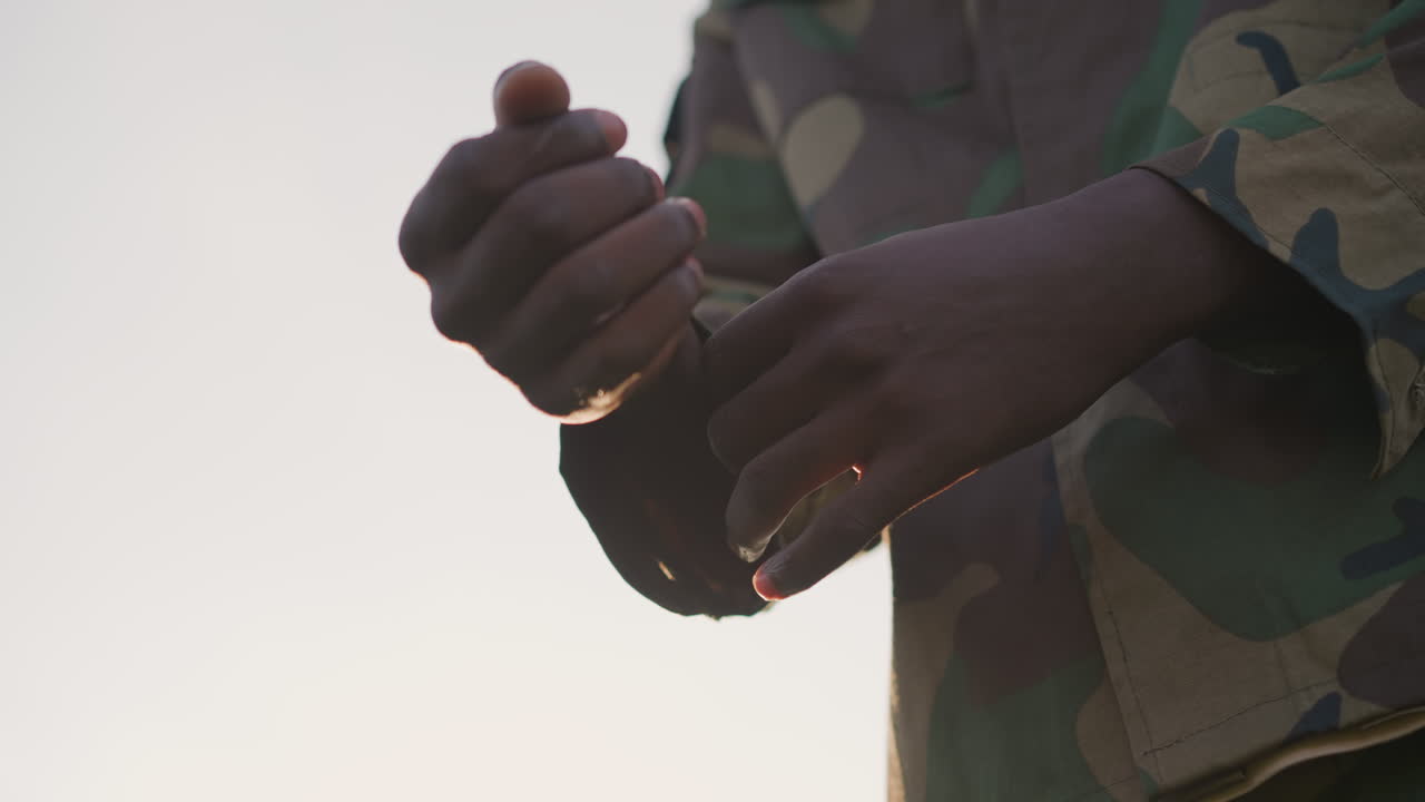 Early Morning Military Discipline, Focused Soldier Preparing During Sunrise Drills, Disciplined Soldier Carefully Prepares For Training By Rolling Up Sleeve At Early Morning In Field