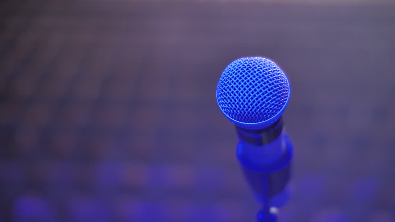 Microphone on stand close up, blurred empty theater audience. Arc shot