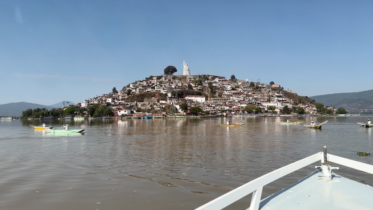 Patzcuaro Gölü'nde, yamaç evleri ve heykeliyle Janitzio Adası'na yaklaşan tekne manzarası.