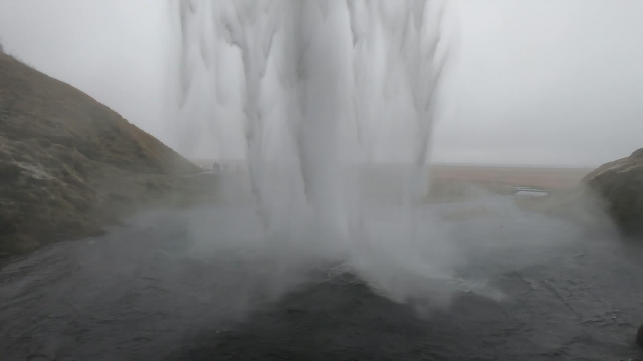 아이슬란드의 셀야란드스포스(seljalandsfoss) 폭포 뒤에서 한 여성이 떨어지는 물의 아름다움과 힘에 감탄하는 영화 장면