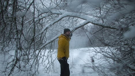 heavy snow falling on man standing under snow-covered trees, slow motion