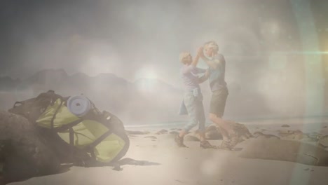 happy caucasian senior couple hiking, having a dance on beach, over fast moving clouds and sunlight