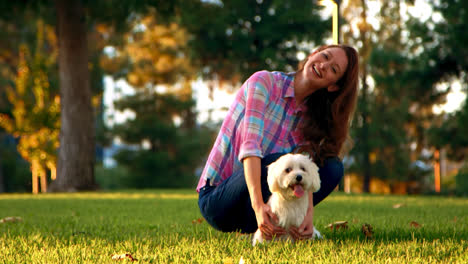 Frau-Streichelt-Weißen-Hund-Im-Park-Und-Schaut-In-Die-Kamera