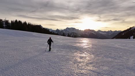 aerial tracking shot of mountaineer walking on snowy slope during sunrise in the morning - swiss alps, amden