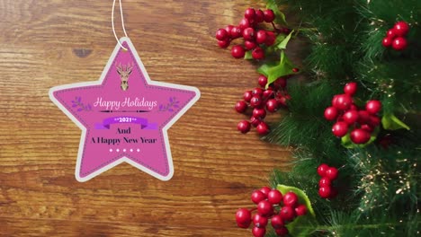 Animation-of-happy-holidays-christmas-text-on-star-shape-tag-over-decorations-on-wooden-background