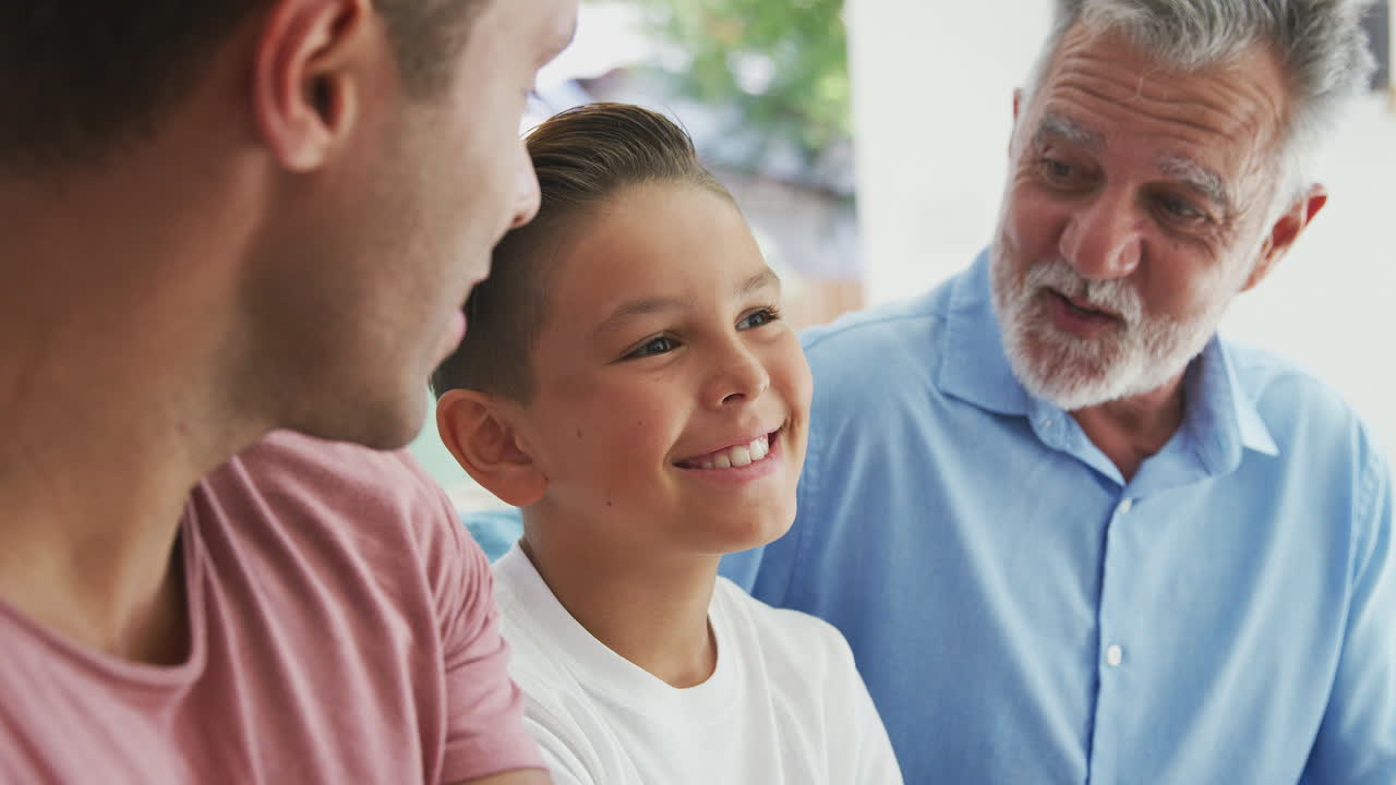 다세대 남성 히스패닉 가족이 집에서 소파에서 함께 이야기하고 웃고 있습니다.