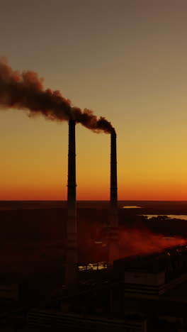 air pollution. dark smoke goes from industrial pipes at sunset. silhouette of harmful factory near the river against the setting sun. vertical video