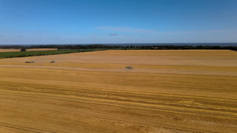 three-combine-harvester-and-tractor-working-on-field-during-harvesting,-in-background-wide-sea,-big-area-of-nature-environment