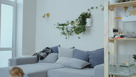 A-4-years-old-boy-with-white-hair-and-a-blue-shirt-jumps-and-smiles-on-the-sofa.-Fun-and-baby-at-home.-Prank-and-pampering