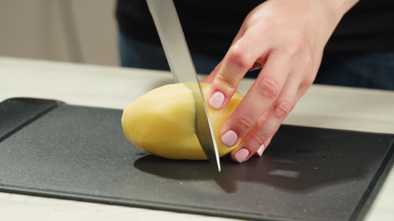 Woman cutting potato on table in kitchen. High quality 4k footage