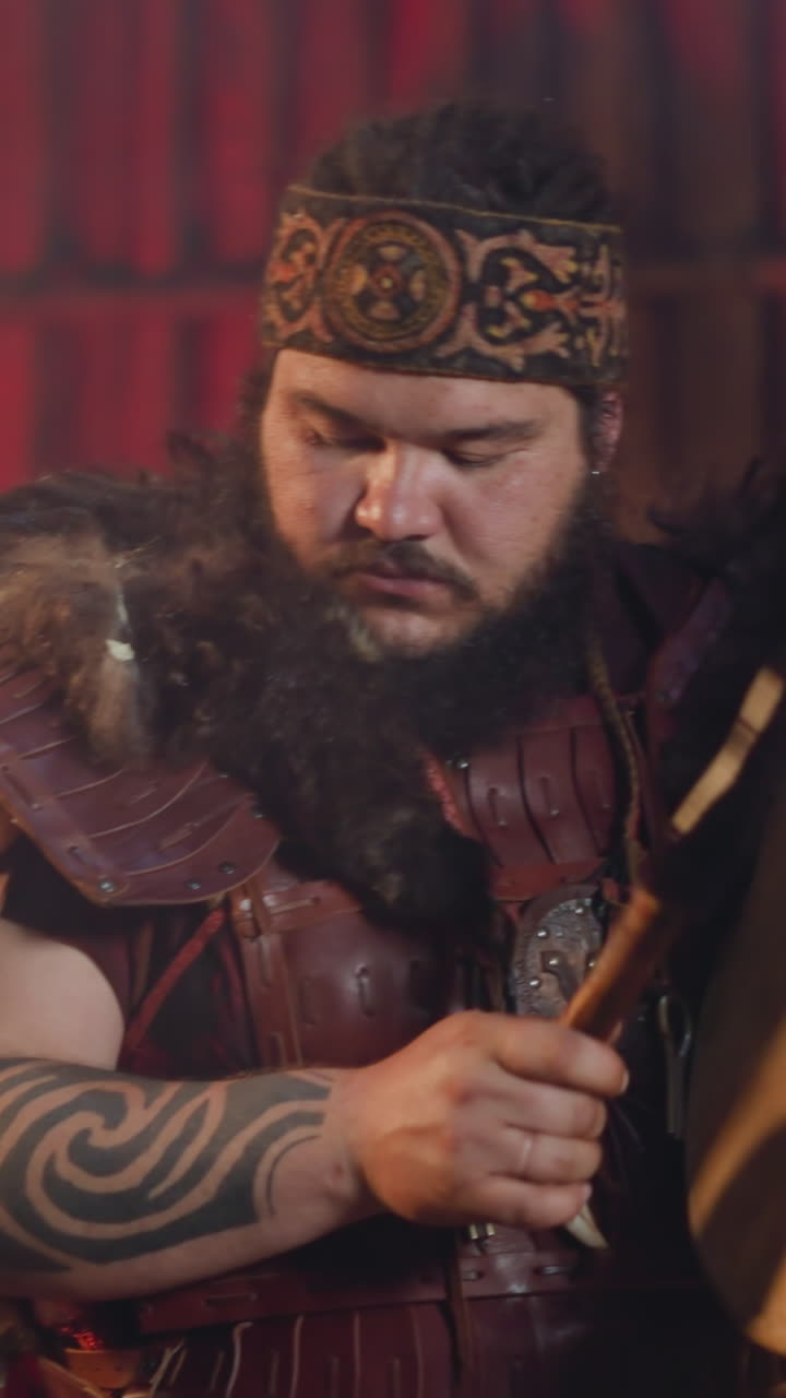 Asian man with tattooed arms conducts evil spirits placating with shamanic drum in ail closeup. Festival of Siberian local culture and traditions