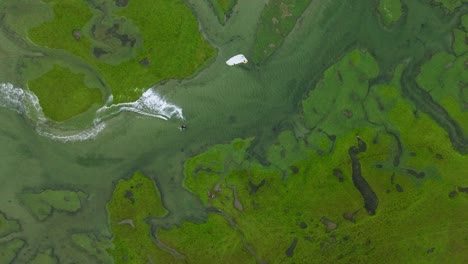 Vista-Aérea-De-Pájaro-De-Un-Practicante-De-Kitesurf-Que-Atraviesa-El-Pequeño-Delta-Del-Río-Con-Hierba-Verde-Brillante-Y-Agua-Clara