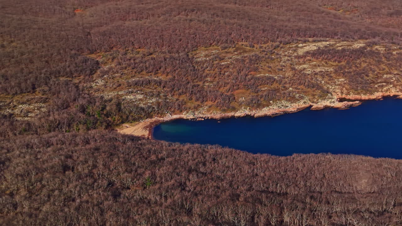 Exploration of a blue lake surrounded by dry trees and rocky terrain in an outdoor area during a clear day