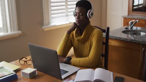 mujer afroamericana que usa auriculares usando una computadora portátil mientras trabaja desde casa