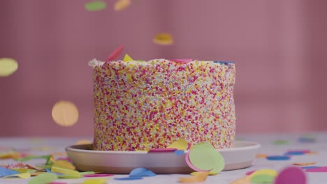 studio shot of paper confetti falling on birthday cake covered with hundreds and thousands decorations 1